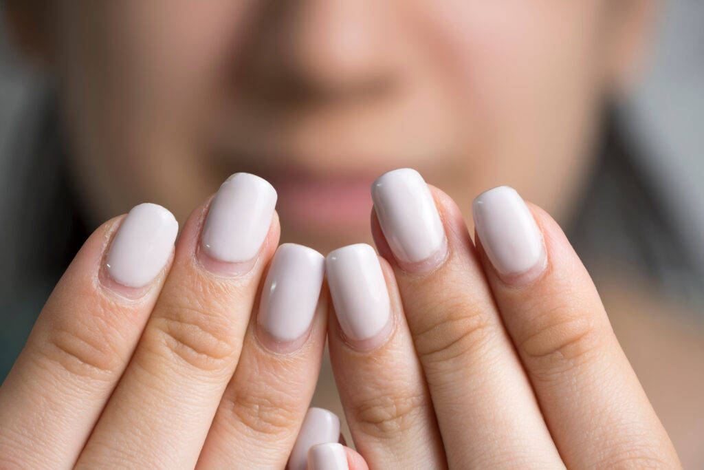 Uñas de una mujer con la cara de fondo